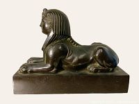 Right-side profile of cast metal sphinx on rectangular base against neutral background.