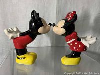 Pair of Mickey and Minnie salt and pepper shakers facing each other on a clear surface, showing front and side profile.