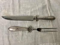 Complete view of the serving knife and fork showing the sterling silver handles and stainless steel utensil parts lying on a cloth surface.