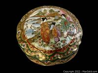 Top view of the signed porcelain covered box showing hand-painted Japanese scene with three women in traditional attire, cranes, flowers, and houses in the background with gold and colored decorative border.
