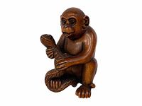 Front angled view of the carved wooden monkey holding a snake, showing detailed facial features and realistic snake texture.