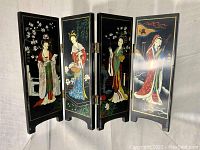 Four-panel black lacquer Japanese folding screen showing detailed paintings of women in traditional kimono and nature themes, standing open to display full artwork.