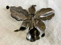 Front view of vintage orchid-shaped sterling silver pin showing detailed petals and curving shapes that mimic orchid flower.
