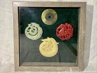 Frontal photo of the framed jade medallions and brass coin, showing all four pieces in wooden frame with dark velvet backing.