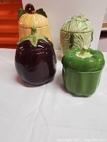 Four ceramic vegetable-shaped jars arranged on a white surface showing the variety of shapes and colors.