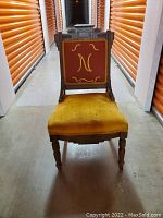 Front view of Eastlake Victorian parlor chair with mustard yellow seat and red fabric back with yellow embroidery.