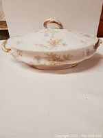 Front-side view of antique Haviland Limoges covered bowl with floral pattern and gold trim, showing scalloped oval shape and scrolled handles.