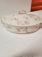 Side view of the closed covered bowl showing floral pattern and gold trimmed handles and lid.