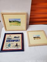 Three framed artworks including one watercolor with greenery and house, and two smaller framed watercolors and embroidery.