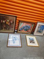 All five framed floral artworks arranged leaning against a wall with orange striped background