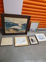 Full group of six framed sailboat artworks placed on floor against orange storage unit door.