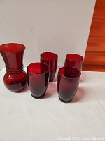 Set showing one red glass vase with flared top and four matching tumblers in deep ruby red color