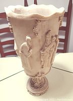 Front view of vase showing carved Asian figures and scalloped top rim.