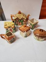 Overview of all six cottage-shaped ceramic pieces showing teapot, creamers, and small containers with rustic paint and textured handles and roof details