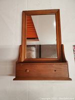 Wooden framed rectangular mirror showing the front with shelf and drawer below. One drawer knob is missing.
