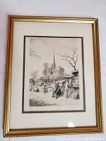Framed vintage black and white pen and ink drawing of Paris street scene with Notre-Dame Cathedral in the background, showing market stalls and people in the foreground.