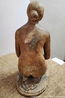 Back view of vintage kneeling nude female sculpture showing hair in bun and oval base with signs of wear.