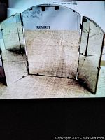 Front view of vintage trifold mirror with three mirror panels spread open on a carpeted floor showing the mirror surfaces and slight imperfection at bottom of center mirror.