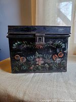 Front view of black metal document box with hand painted floral designs and latch.