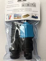 Photo of packaged inflatable pump adapter with black valve parts and blue valve nozzle inside clear plastic, showing front packaging and product.
