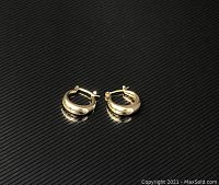 Small gold hoop earrings with latch back closure on a black surface.