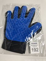 Photo showing pair of pet grooming gloves sealed in clear plastic packaging with blue silicone bristle side facing up and black mesh cloth on back.