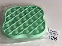 Light green silicone push pop bubble sensory toy in plastic packaging on a white surface.