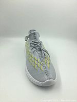 Front and top angled view showing knit upper, lace-up closure, and yellow scale-like design elements on sides.