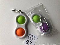 Two key chains with colorful silicone bubbles, one pack sealed in plastic, placed next to a MaxSold tag.
