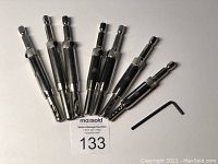 Eight center drill bits with hex shanks and one black L-shaped hex key on a white background, item lot tag 133 in front.