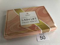 Front and top view of unopened Essy Naturals Lash Lift Eyelash Perm Kit in peach, white, and gold design.