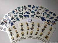 Photo showing 14 sheets of temporary tattoos including Minions and sharks designs arranged in two rows. Clear packaging showing number and variety.