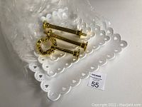 Three white ceramic or porcelain square plates with scalloped edges and three gold-tone metal posts and decorative handle piece placed on top.