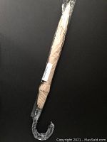 Full view of the tan umbrella wrapped in plastic with curved handle visible