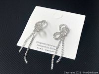 Pair of silver tone rhinestone bow and dangle earrings on white card showing original handmade and Korean design.