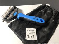 Pet grooming shedding tool with blue and black handle and black carrier pouch laid on white surface.