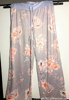 Photo of full length gray wide leg pajama pants with peach and white floral print, hanging for display.