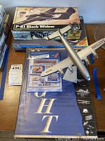 Full lot photo showing MPC P-61 Black Widow box, assembled plane model, aviation book, and postcards.