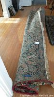 Rolled vintage floral area rug on wooden floor showing overall design and rolled edges.
