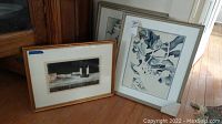 Two framed artworks on floor including a W.B. Hansen print and a watercolor framed in silver metal frame.