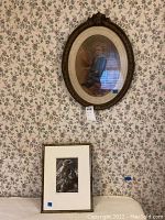 View of oval portrait of child artwork and religious print beneath it, displayed against floral wallpaper.