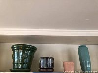 Photo displaying five ceramic and glazed planters, bowls, and vases in varying sizes and colors arranged on a shelf.