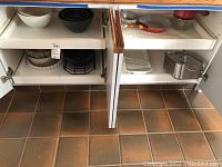 View of cabinet showing white ceramic baking dish, metal roasting pan with lid, and metal pans on shelves