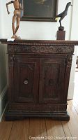 Front view of small antique style wooden cabinet with two doors and top drawer, displaying carved decorative elements and dark wood finish.
