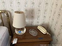 Photo showing crystal oval lamp with fabric shade, glass candy dish, and beige Radio Shack phone on wooden surface.