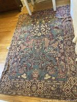 Full view of the rectangular decorative rug spread on a wooden floor showing the overall design and condition.