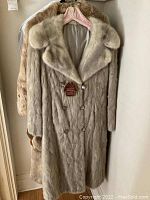 Three fur coats hanging in closet, showing a light blonde coat with double-breasted buttons and wide collar.