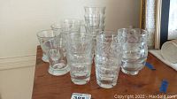 Front view of eleven assorted clear glasses arranged on a wooden surface, various shapes and textures visible.