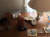 Table with lamp, clay canister, ashtray, coasters, small white dish and a bag with contents.