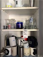 Photo showing multiple glassware items including tall and short glasses and several mugs arranged inside a cabinet shelf.